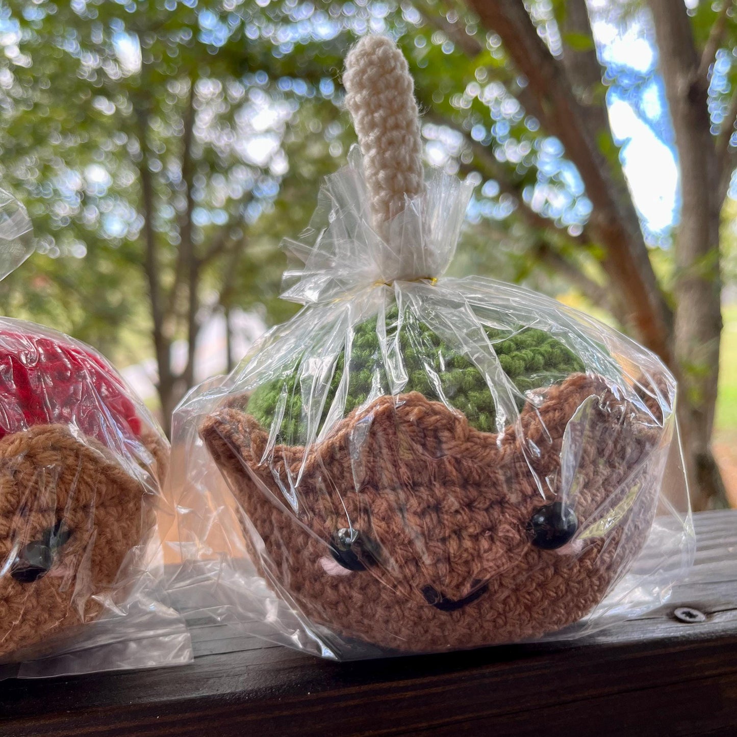 Crocheted candy apple figures wrapped in clear plastic with a natural outdoor background