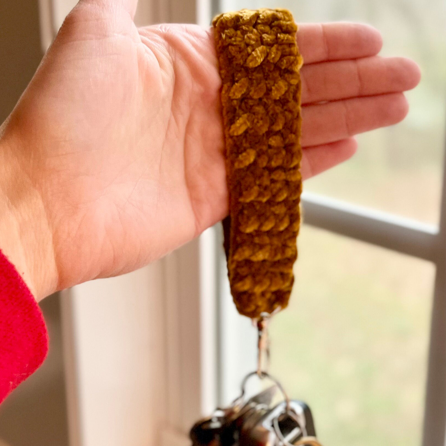 Hand holding a crocheted brown keychain with a blurred background
