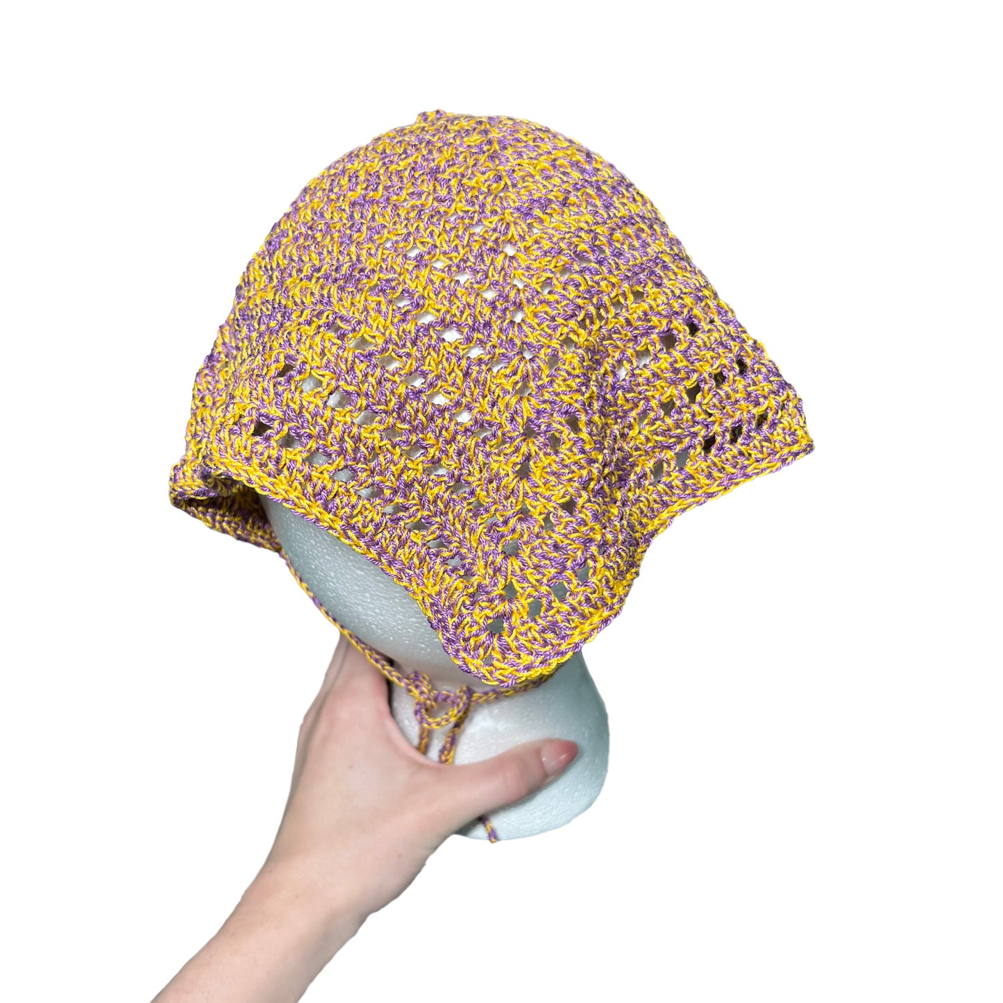 Hand holding a purple and yellow crocheted bandana on a white background