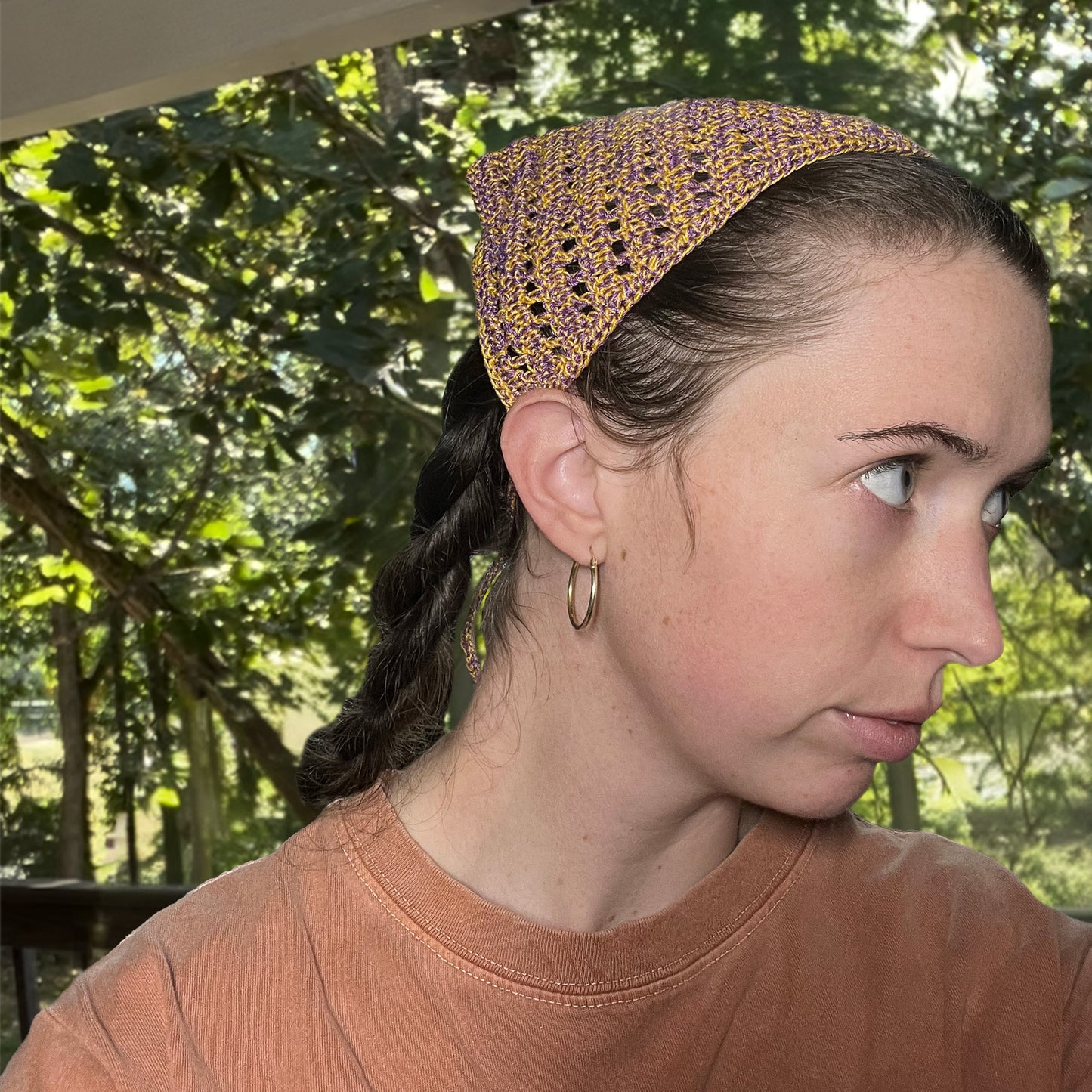 Woman wearing a crocheted bandana outdoors with greenery in the background