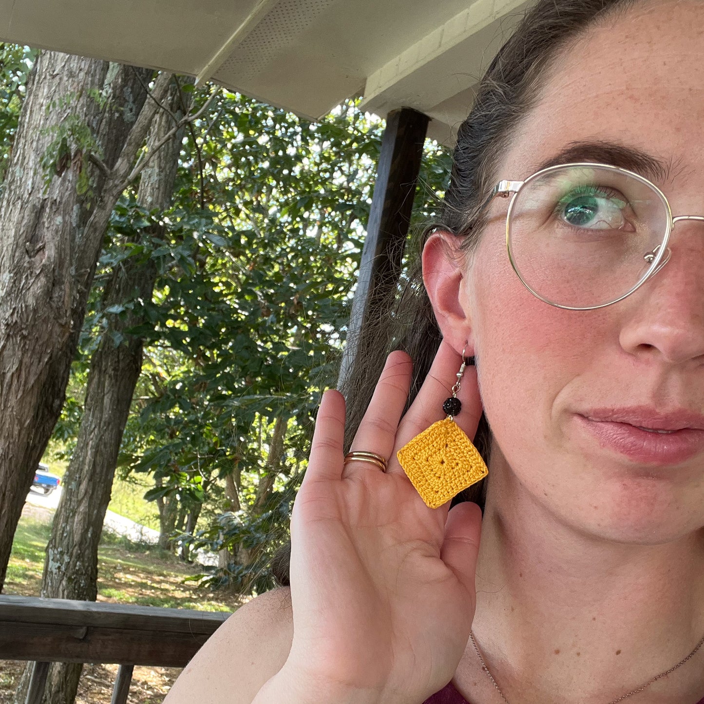 Person wearing a yellow square earring outdoors with trees in the background