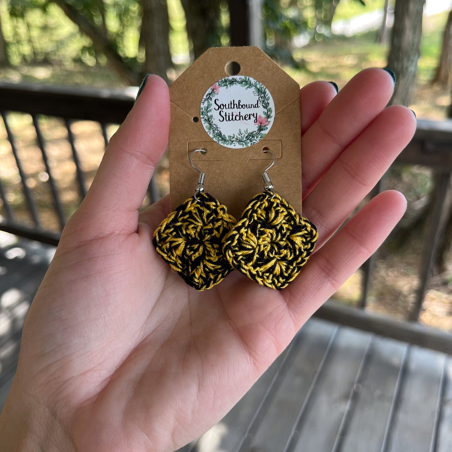 Hand holding a pair of black and yellow patterned earrings on a Southbound Stitchery card.