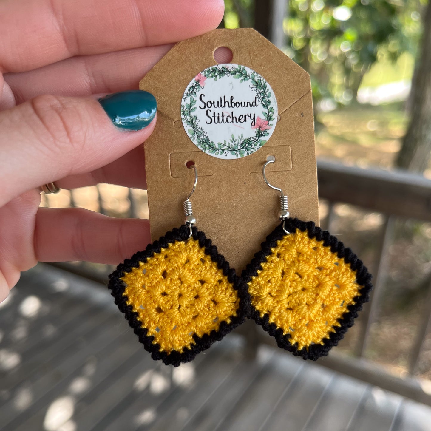 Yellow and black crochet earrings on a Southbound Stitchery card held by a hand.