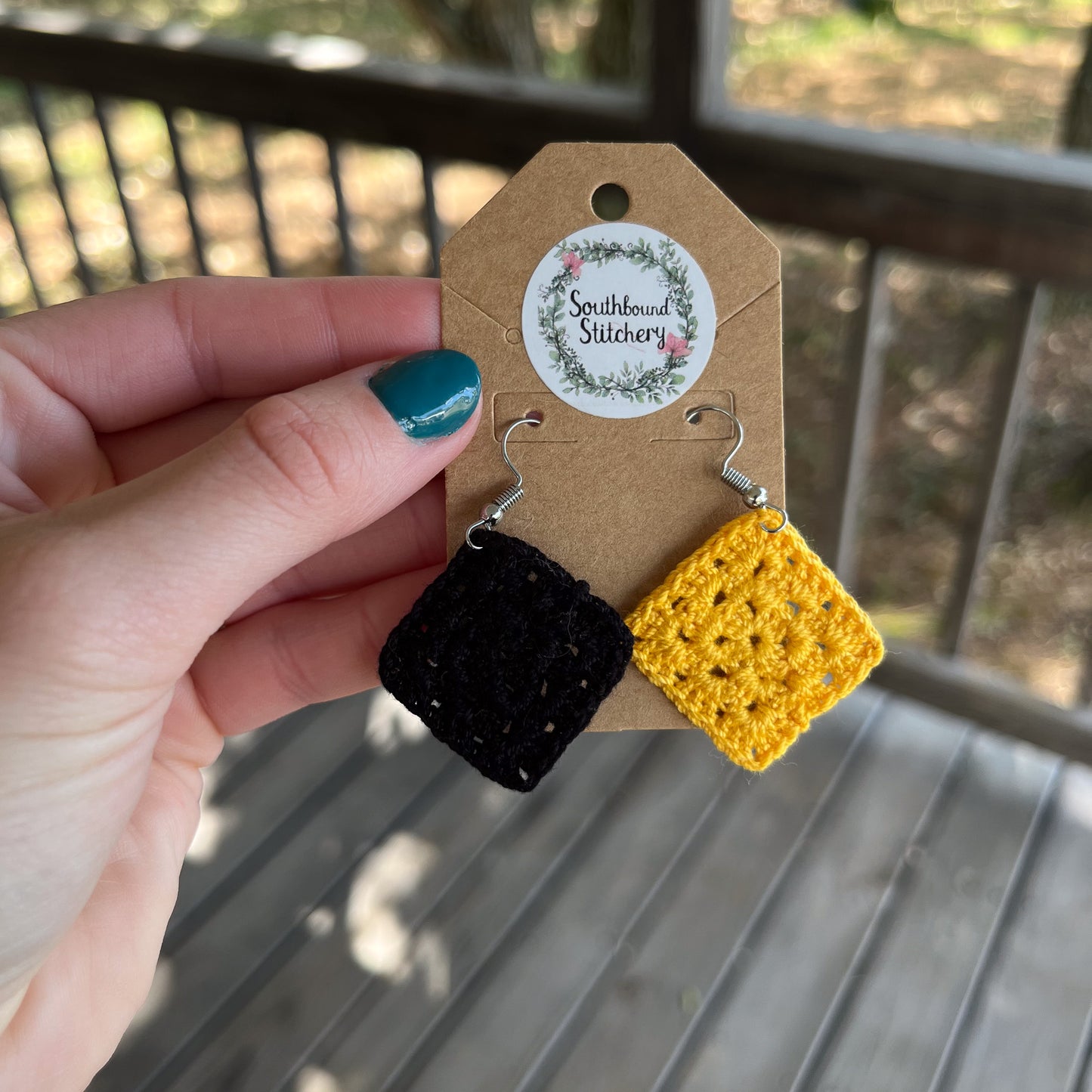 Hand holding a pair of black and yellow crochet earrings on a Southbound Stitchery card.