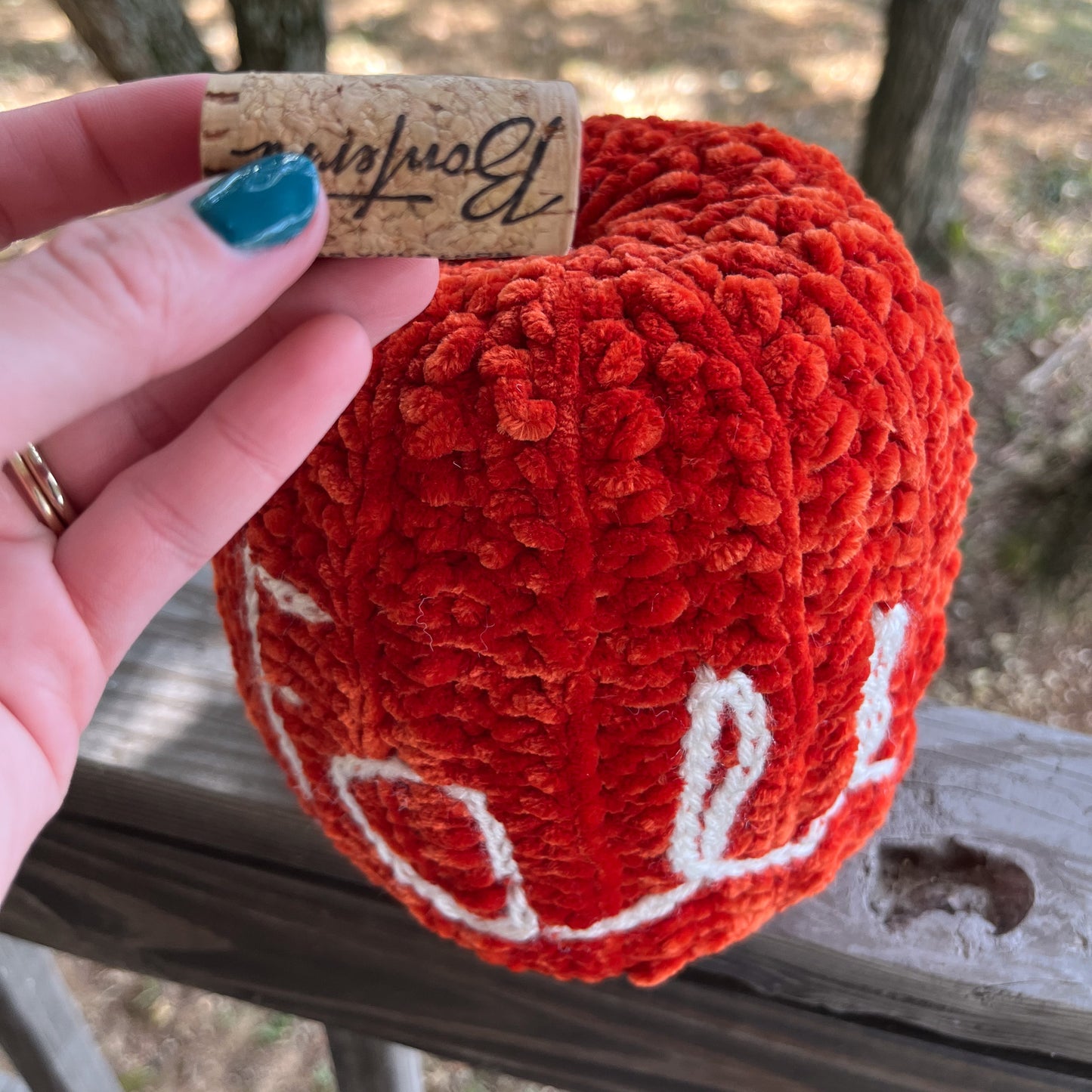 Orange crocheted pumpkin with a wine cork held by a hand outdoors