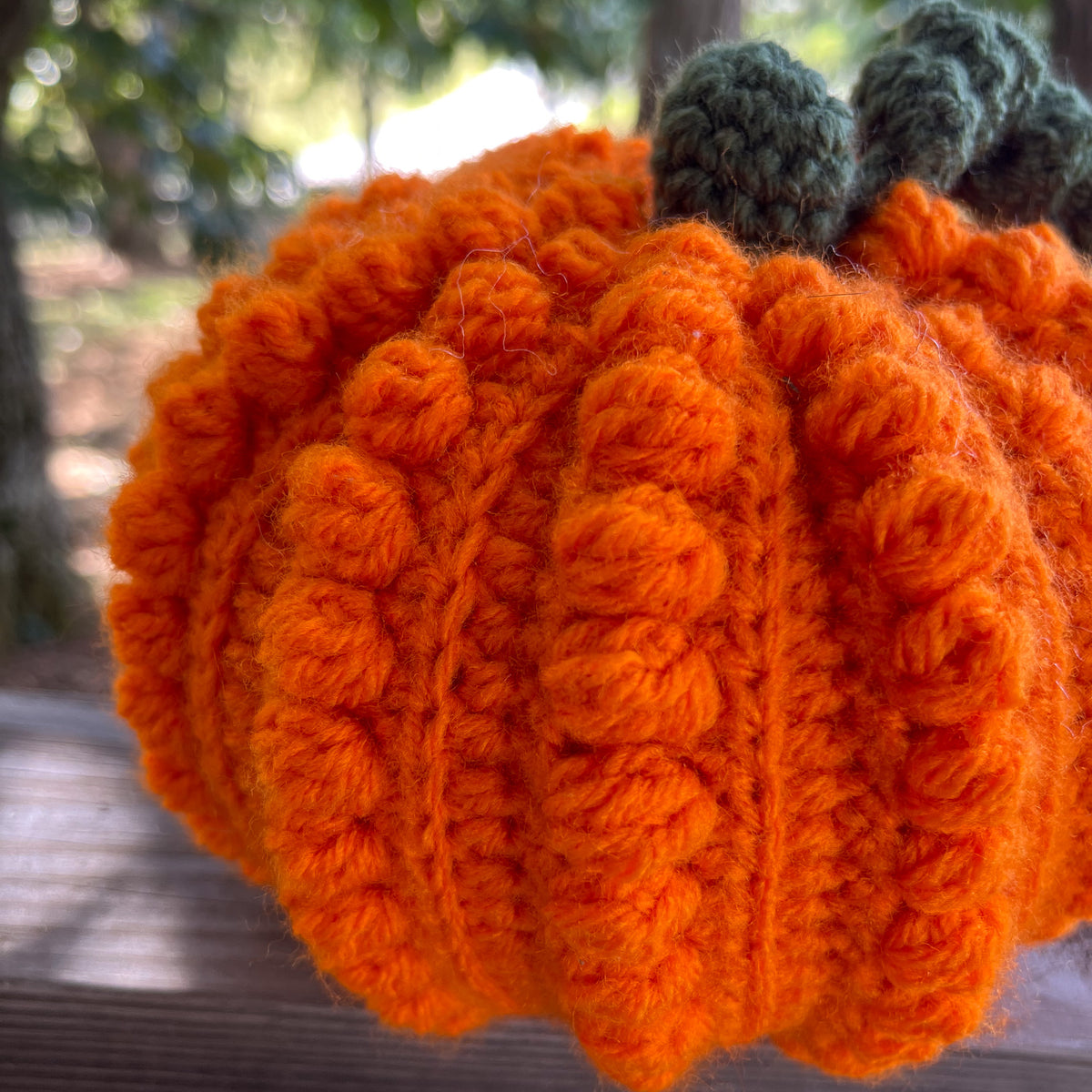 Crocheted orange pumpkin with green leaves against a blurred natural background