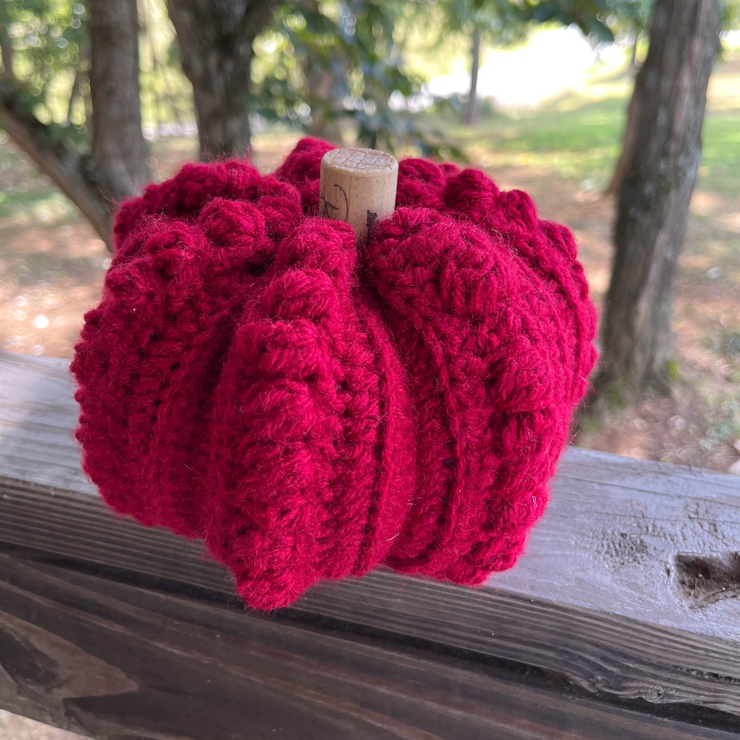 Red Crocheted pumpkin on a wooden surface with a natural background