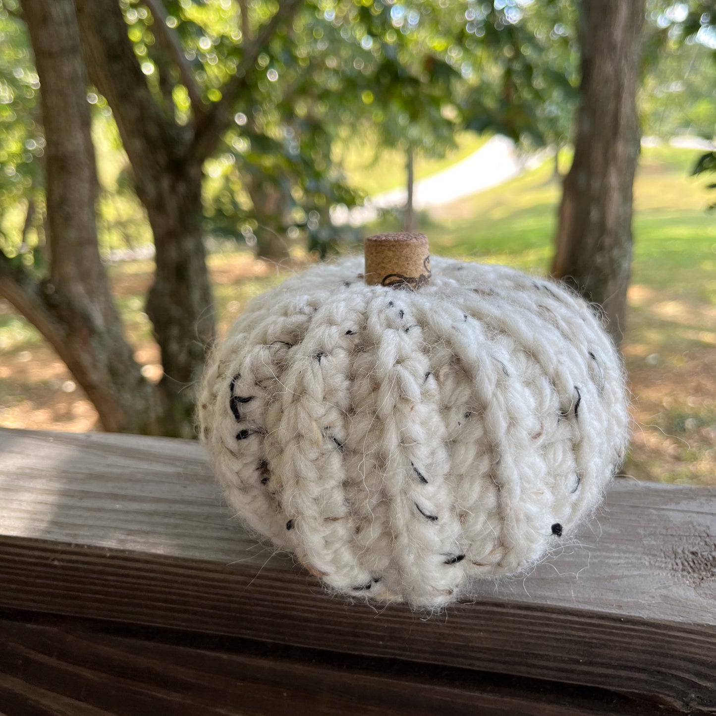 Crocheted pumpkin decoration on a wooden surface with a natural outdoor background