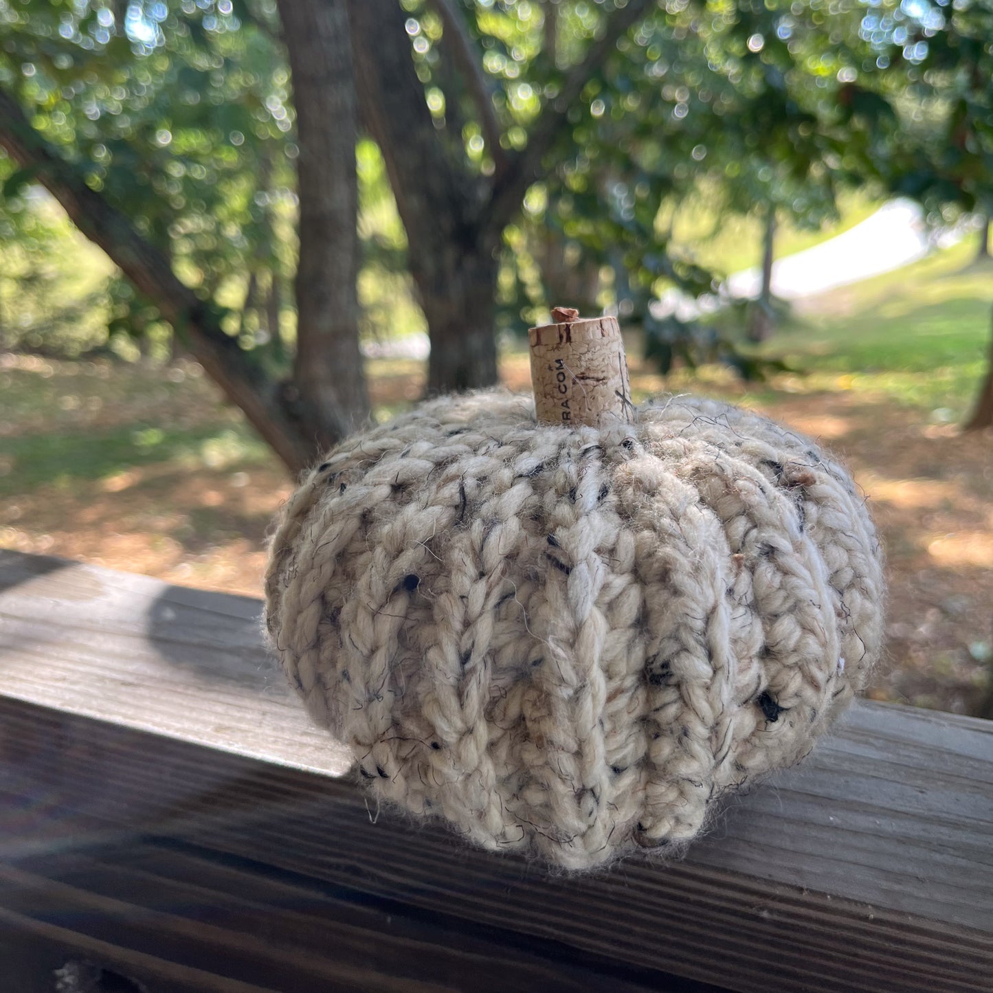 Crocheted pumpkin decoration on a wooden surface with a natural outdoor background