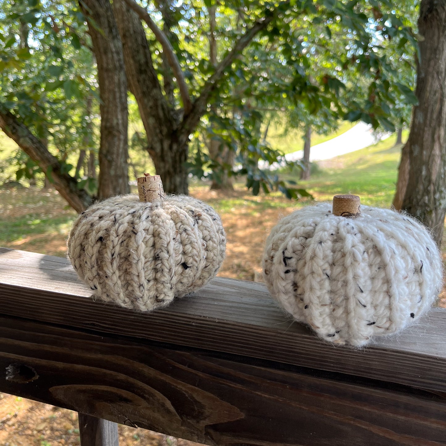 Two Crocheted pumpkins on a wooden surface with a natural outdoor background