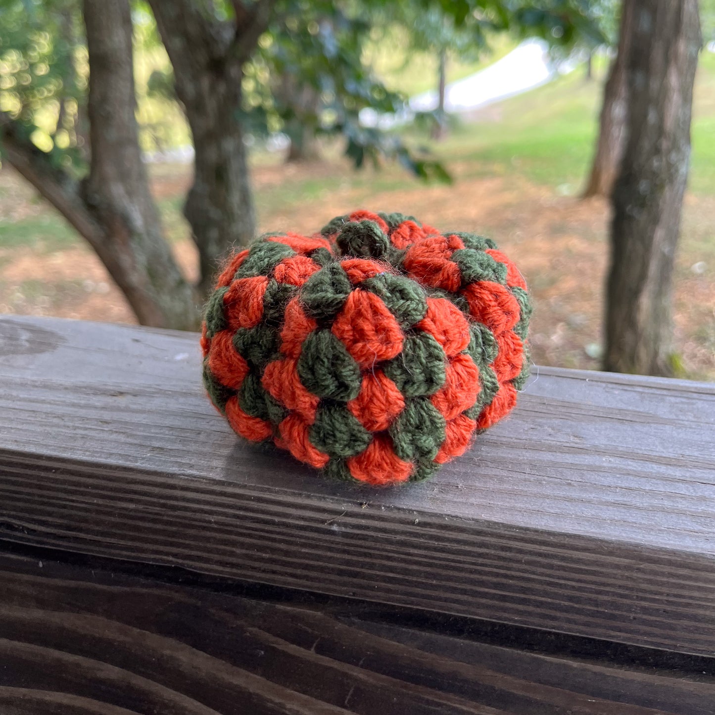 Green and orange granny square stitch crocheted pumpkin on wooden ledge outside