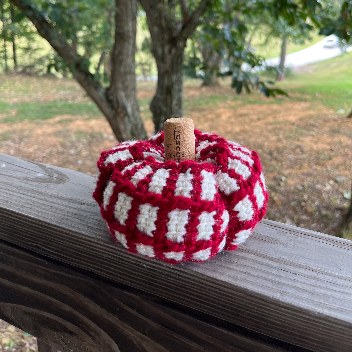 Red and white crochet pumpkin on wooden ledge outside