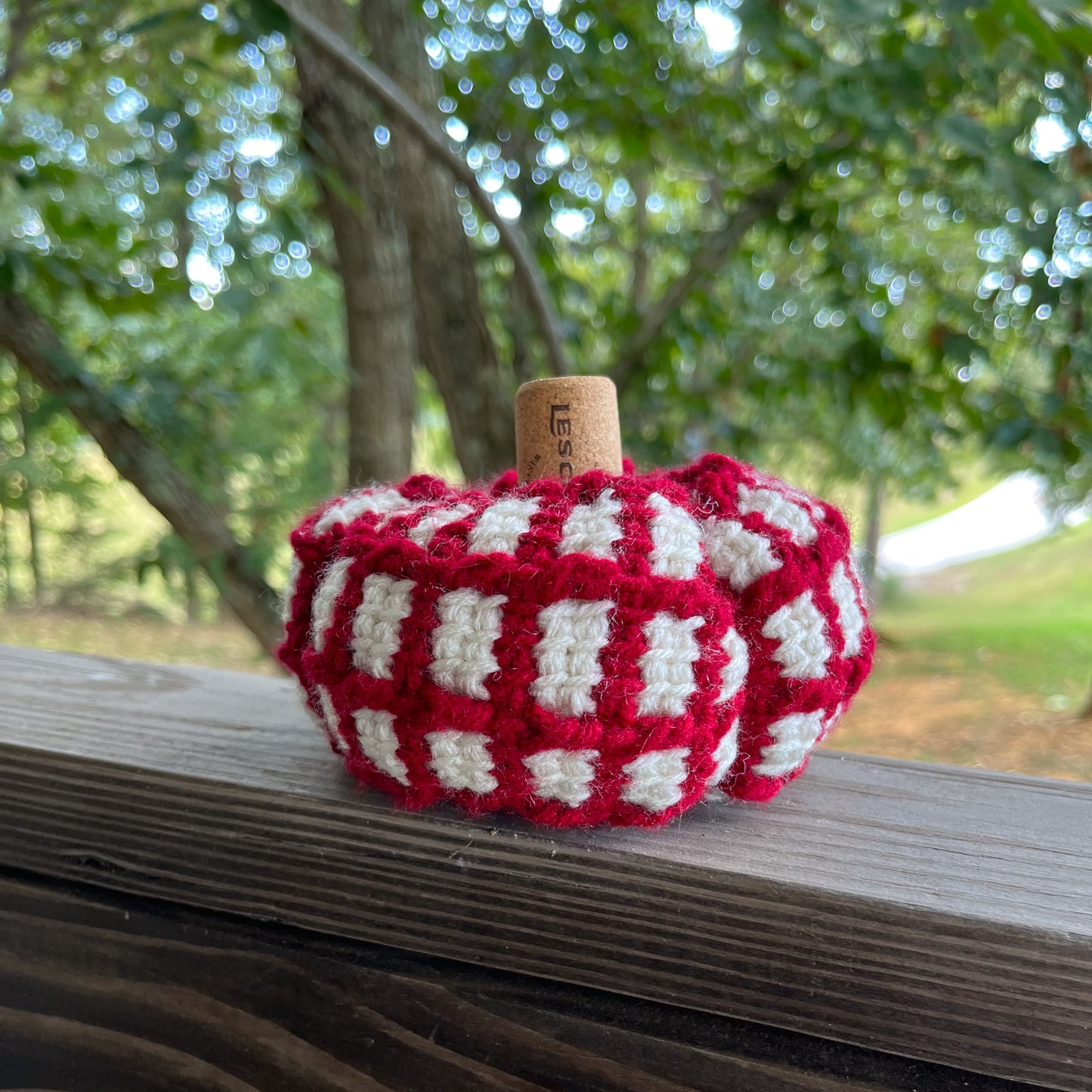 Red and white crochet pumpkin on wooden ledge outside
