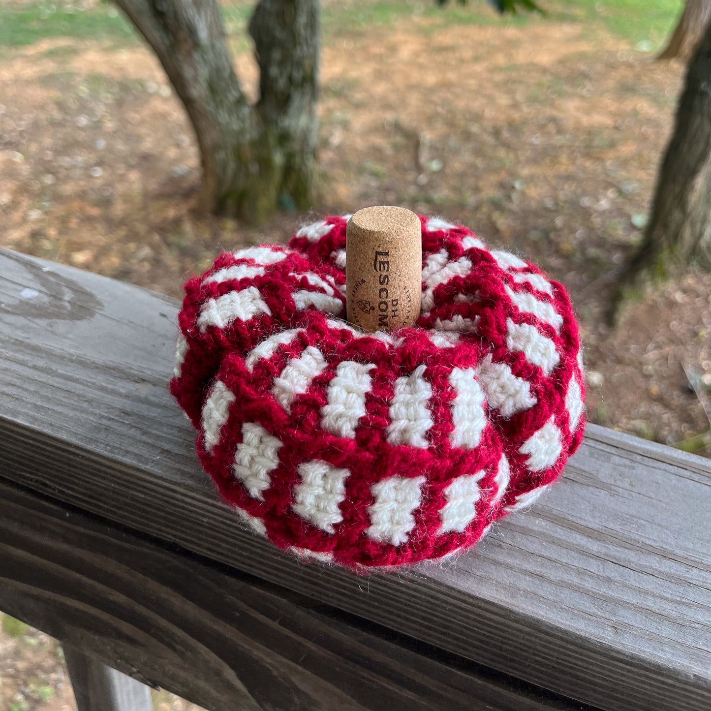 Red and white crochet pumpkin on wooden ledge outside