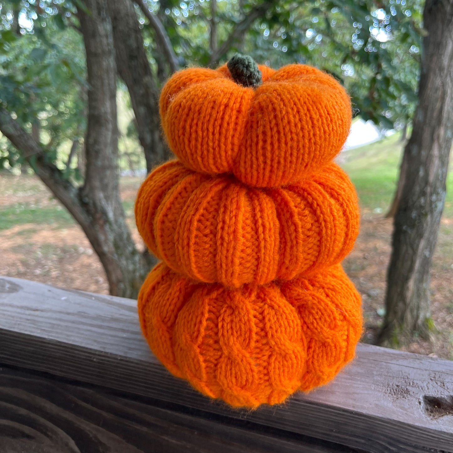 Stack of orange knitted pumpkins on a wooden surface with a natural background