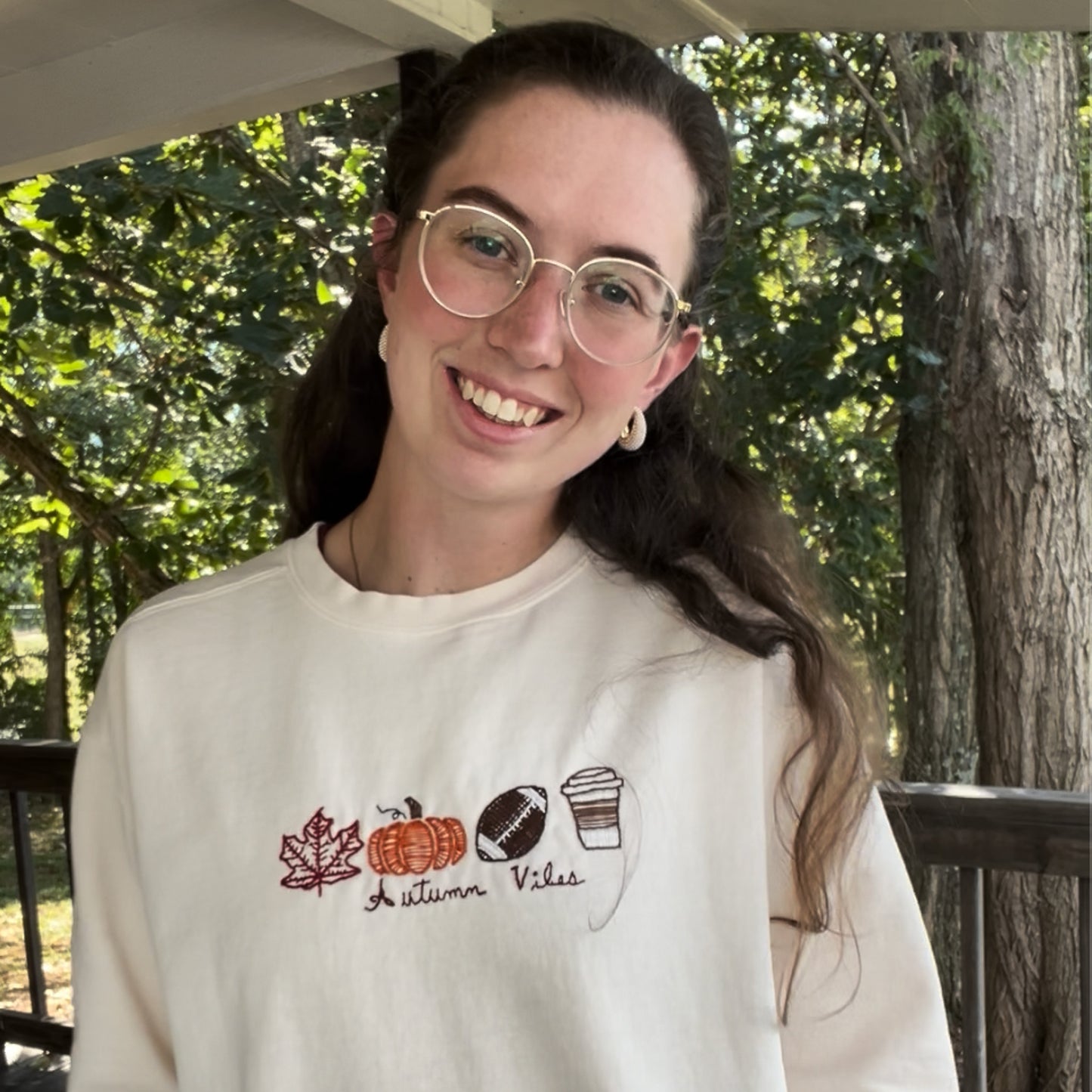 Person wearing a white sweatshirt with autumn-themed designs outdoors.