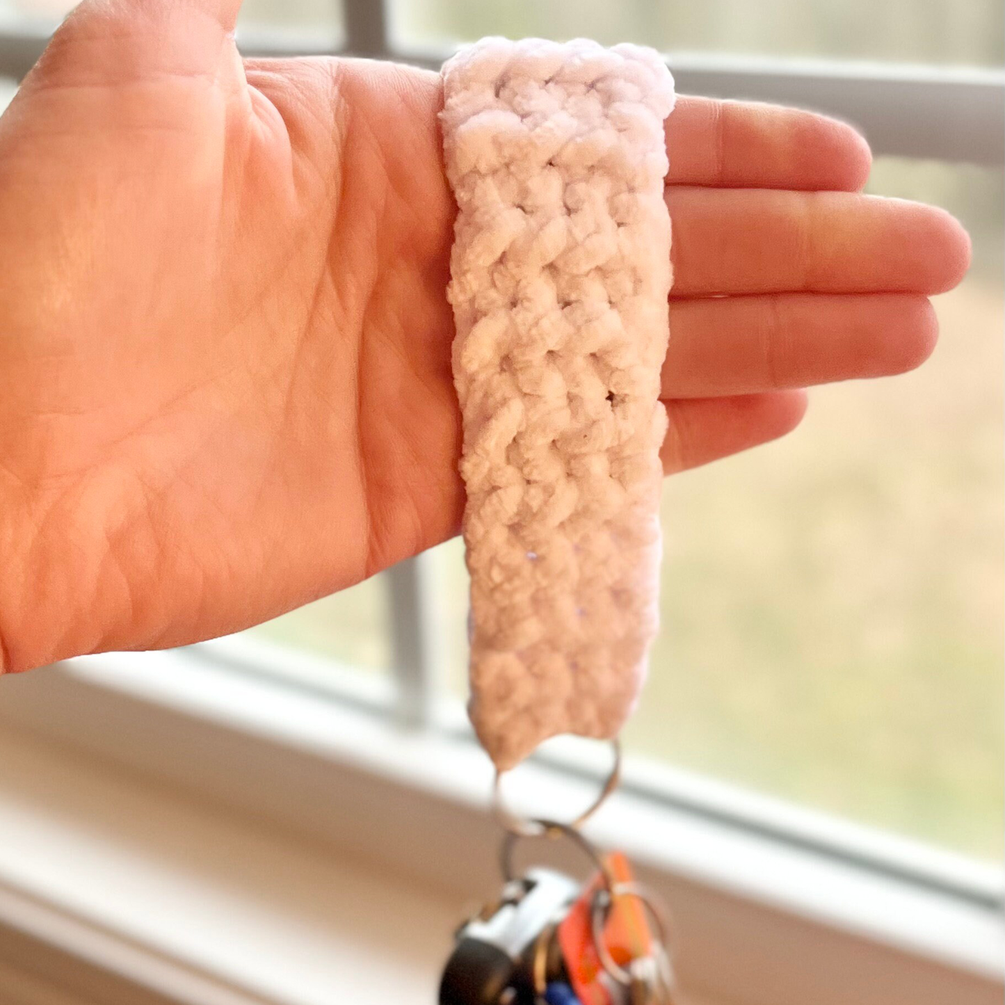 Hand holding a crocheted white keychain with a blurred background