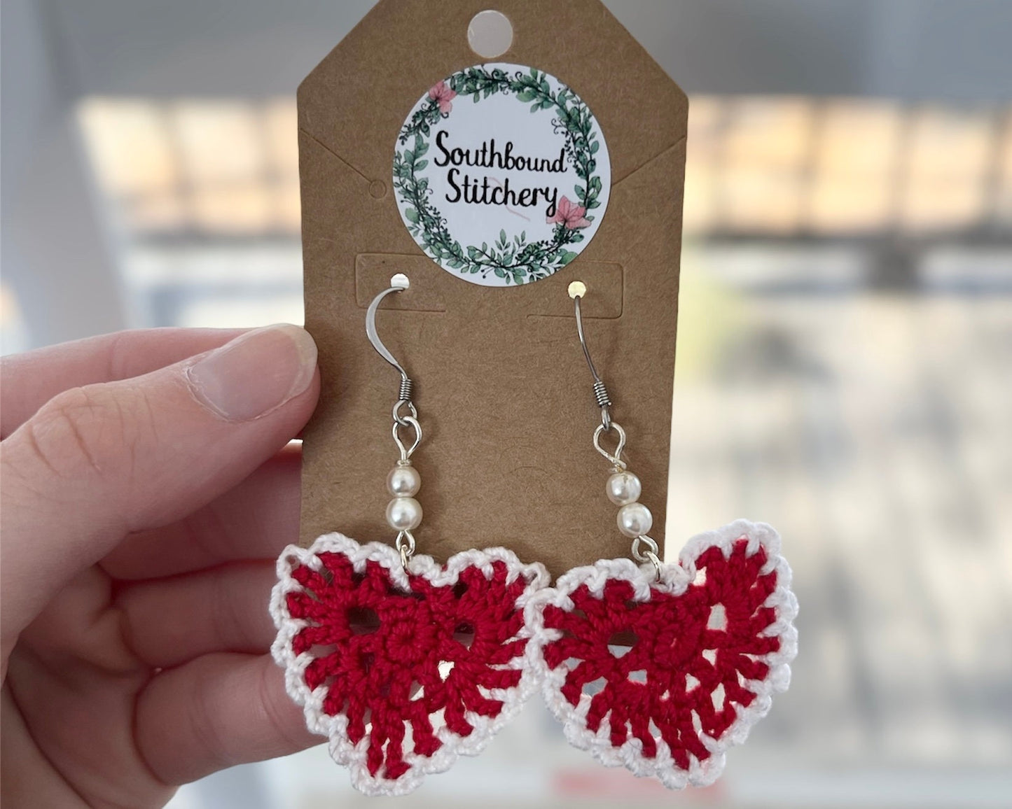 Red and white crochet earrings on a Southbound Stitchery card.