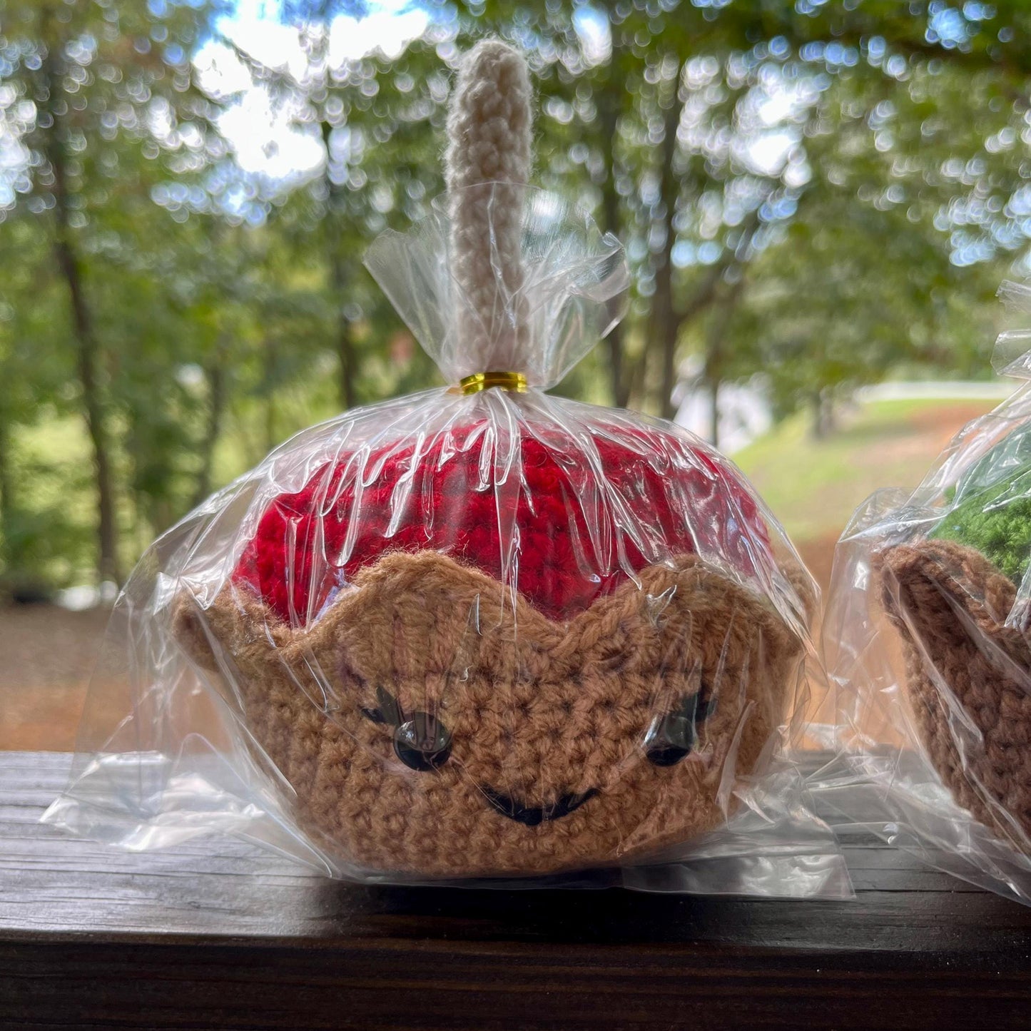 Crocheted apple with a face in clear plastic wrap on a wooden surface with a blurred natural background
