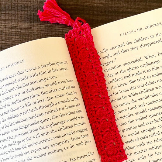 Red crocheted bookmark on an open book with a tassel.