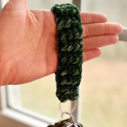 Green crocheted keychain held in a hand against a neutral background
