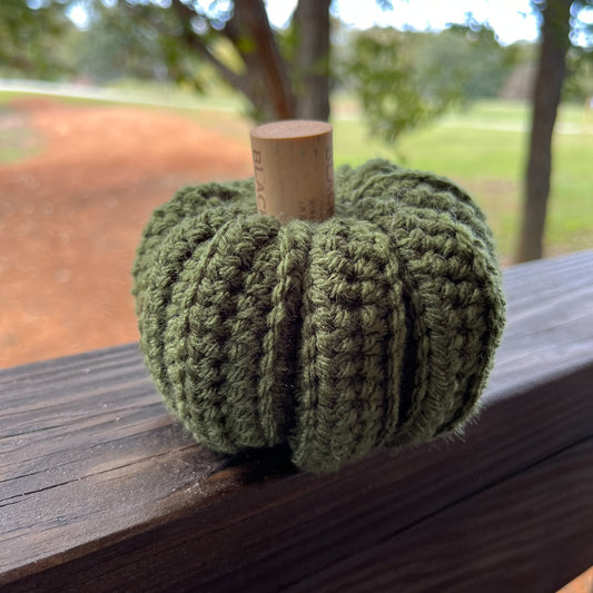 Crocheted green pumpkin on a wooden surface with a blurred outdoor background