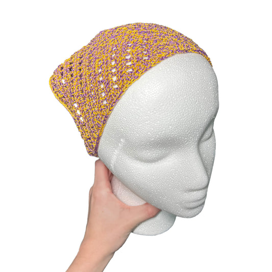 Yellow and purple crocheted bandana on a mannequin head held by a hand against a white background