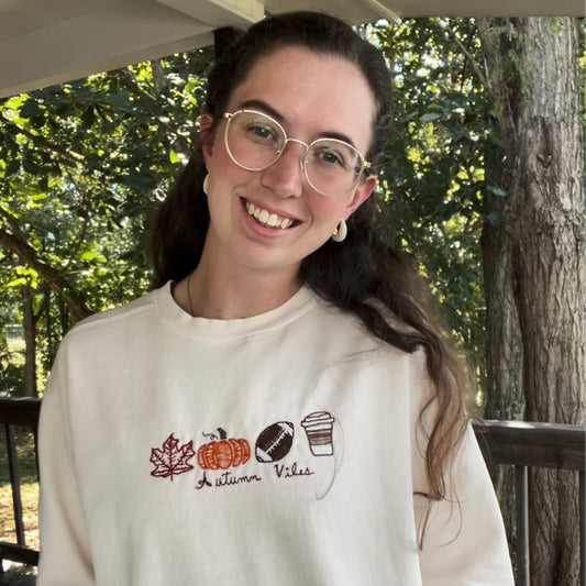 Person wearing a white sweatshirt with autumn-themed designs outdoors.